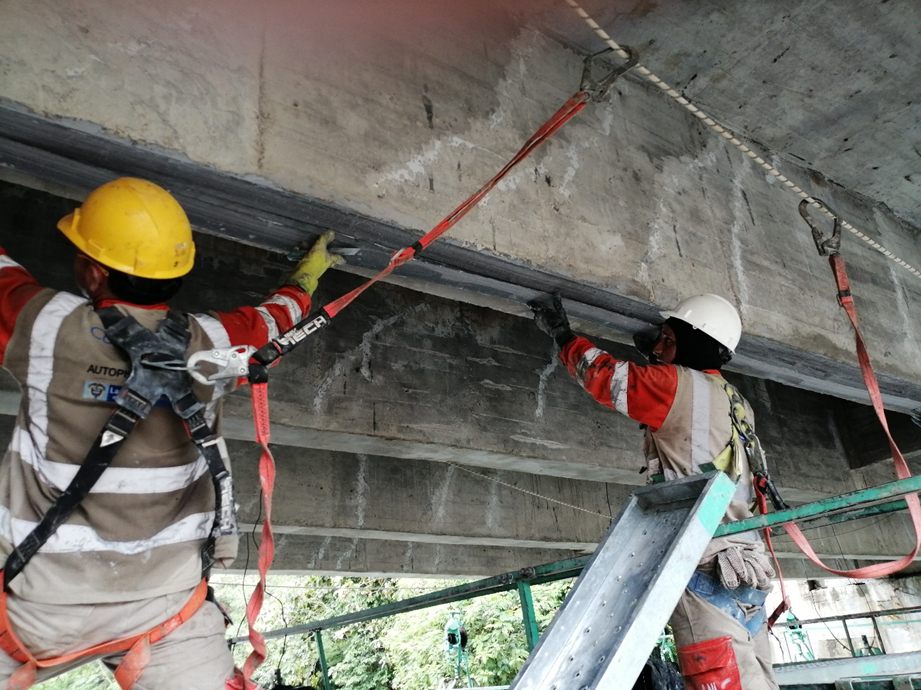 Dos operarios instalando lámina de fibra de carbono bajo el tablero de un puente